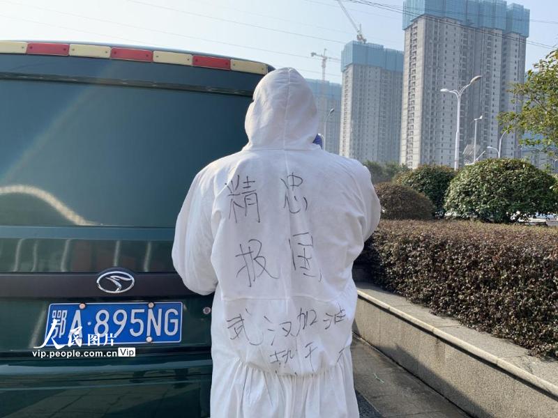 2月22日，武汉客厅方舱医院门口，一辆运输物资的邮政驾驶员防护服上写着“精忠报国”“武汉加油”等字样。（柴选 人民图片）